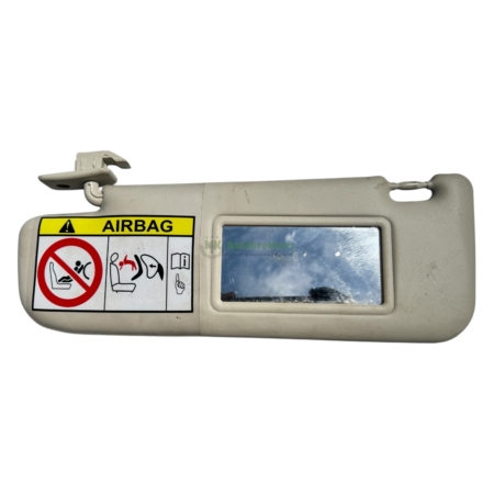 Driver-side sun visor with a bright yellow AIRBAG warning label and safety icons beside a small mirror panel in a beige interior panel.